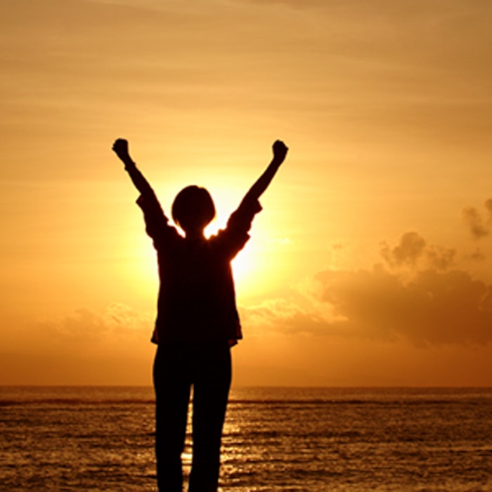 Woman raising her hands at sunrise
