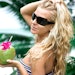 Woman in sunglasses holds coconut in hand.