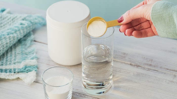 Collagen powder in bowl, glass of water and measure spoon on a white wooden background. Extra protein intake. Natural beauty and health supplement concept.