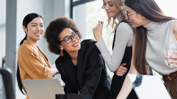 african american businesswoman smiling near multiethnic colleagues near laptop in office