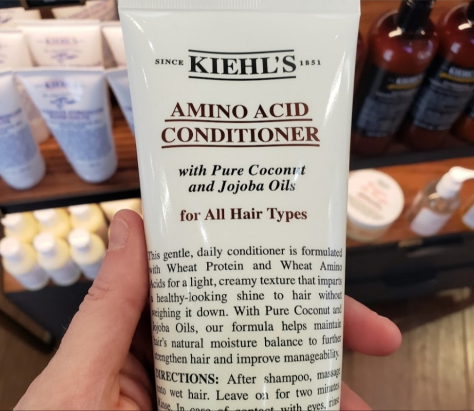 Kiehl's Amino Acid Conditioner held in store in hand background of other products on shelves