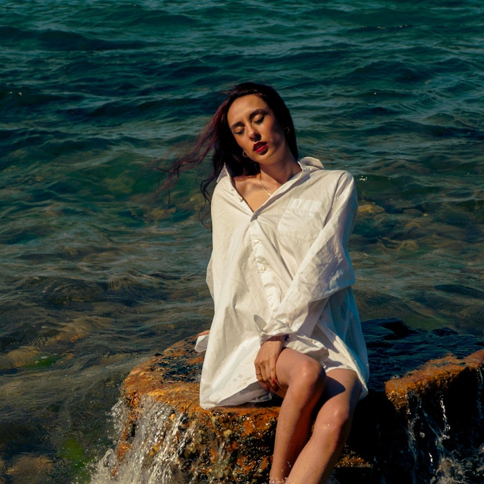 Woman seated on rock in ocean under the sun.