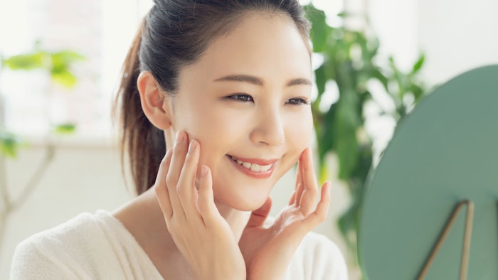 beautiful Asian woman in white robe looking in mirror smiling touching face plants in background
