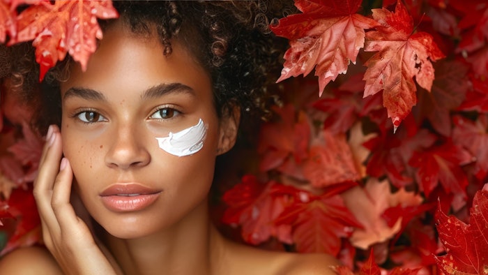 Model with flawless skin applying skincare in an autumn leaves setting for Fall