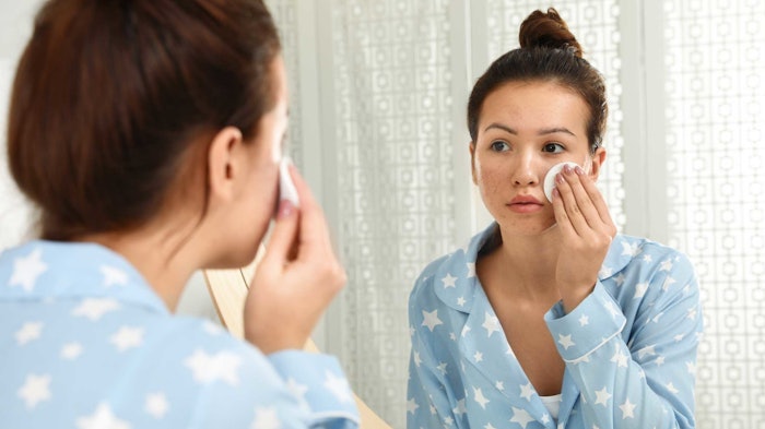 teen-using-acne-skin-care-looking-in-mirror-wearing-pajamas