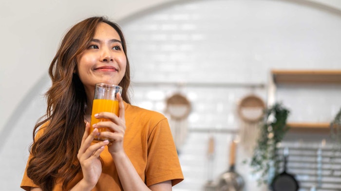 young Asian woman in kitchen drinking orange beverage smiling
