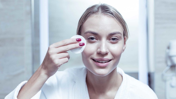young woman looking in mirror wiping face with cotton pad smiling