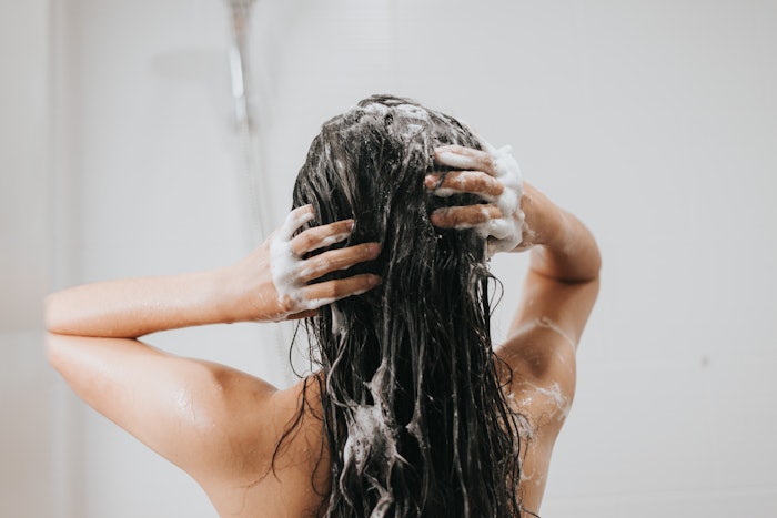 Woman washing hair with shampoo in the shower.