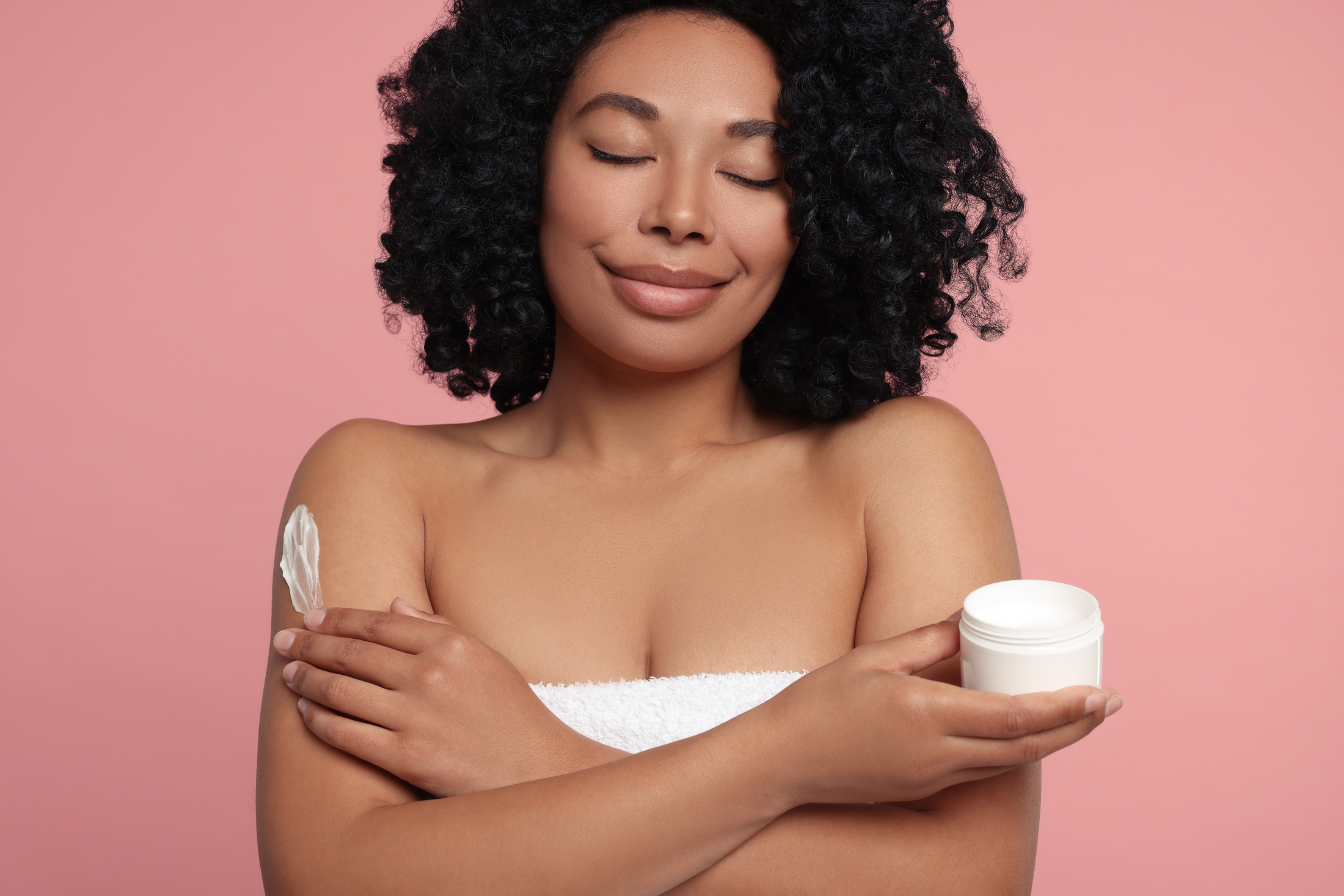 ethnic woman relaxed soothed using body cream pink background