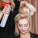 stylist using hairspray on model wearing color cosmetics