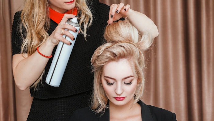 stylist using hairspray on model wearing color cosmetics