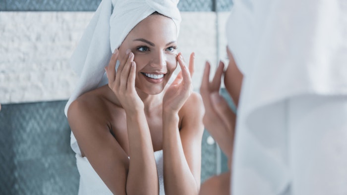 woman mirror applying eye area lotion smiling