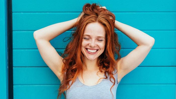 beautiful redhead teal background smiling holding hair up smiling