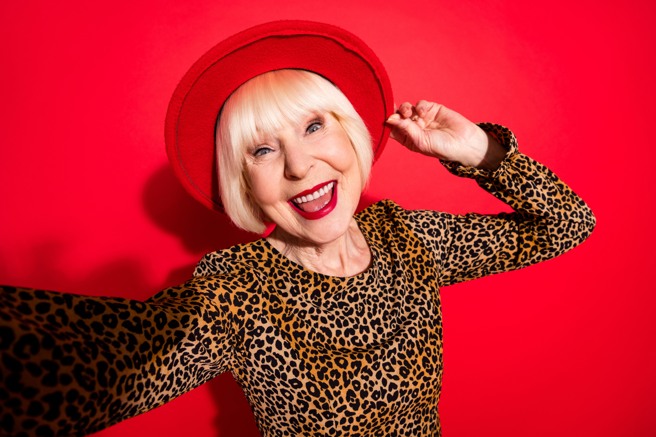 happy mature woman hat leopard shirt red bg