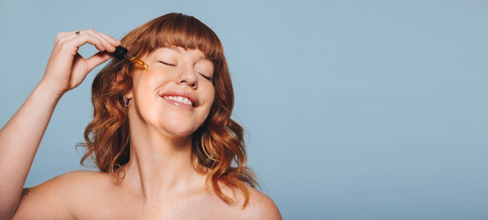 Redhead Applying Facial Serum Happy Emotion Eyes Closed Adobe Stock 540650473