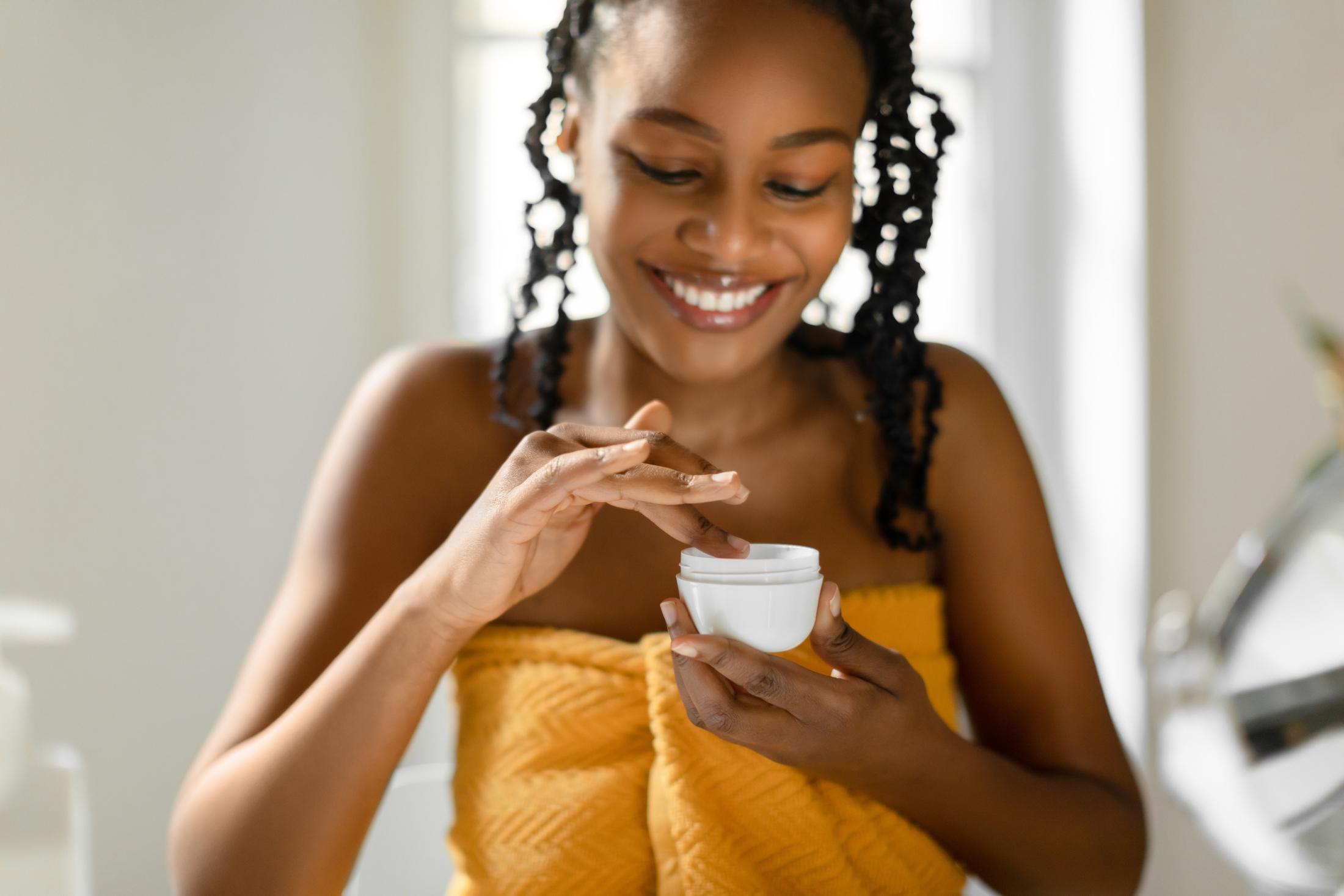 Beautiful Black Woman In Orange Towel Dipping Finger Into White Face Cream Jar Adobe Stock 578686567 (1)