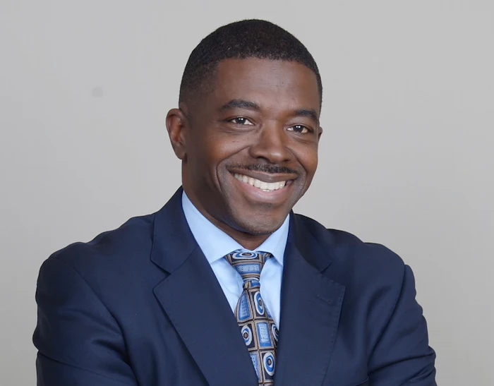 Professional smiling man in navy suit and patterned tie against neutral background