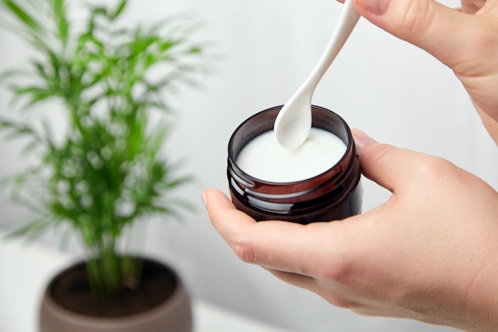 Person Holding Jar Of Skin Cream With Spatula Plant In Background Focus On Hands Adobe Stock 374961360