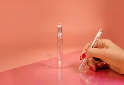 Hand holding clear glass perfume bottle with two additional bottles on coral background