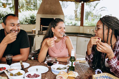 Three friends smiling and enjoying food and drinks together at an outdoor dining table