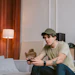 Young man in casual attire gaming on couch with controller in modern living room with speakers and ambient lighting