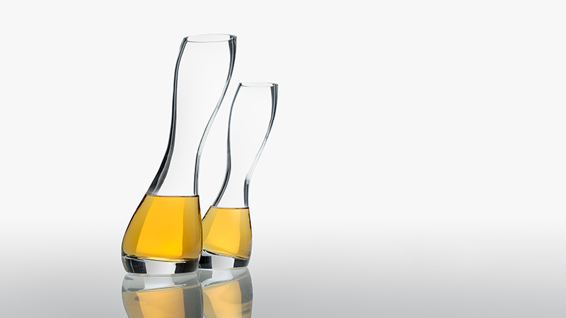 Two elegant glass decanters filled with golden whiskey or spirits, displayed with reflections on a neutral surface.