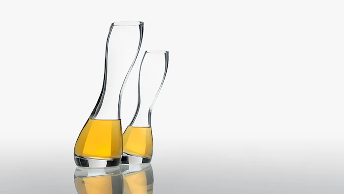 Two elegant glass decanters filled with golden whiskey or spirits, displayed with reflections on a neutral surface.