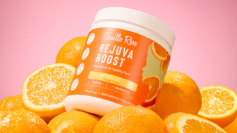 Camilla Raw Rejuva Boost hair supplement jar surrounded by fresh oranges on pink background