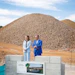 Two professionals stand at construction site with large gravel pile and Fragrance Design Centre signage