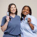 Two smiling women in professional attire posing together against a neutral beige background