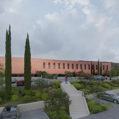 Modern terracotta building with cypress trees, landscaped grounds, and parking area under cloudy sky