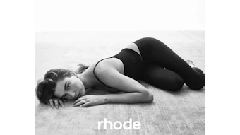 Black and white artistic portrait of woman in athletic wear lying on textured floor with Rhode brand text