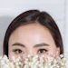 Woman's face partially hidden behind white baby's breath flowers with natural makeup and brown eyes