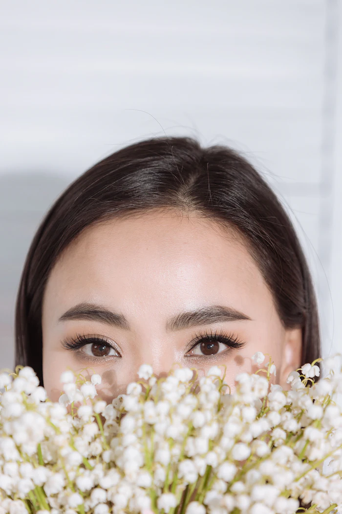 Woman's face partially hidden behind white baby's breath flowers with natural makeup and brown eyes