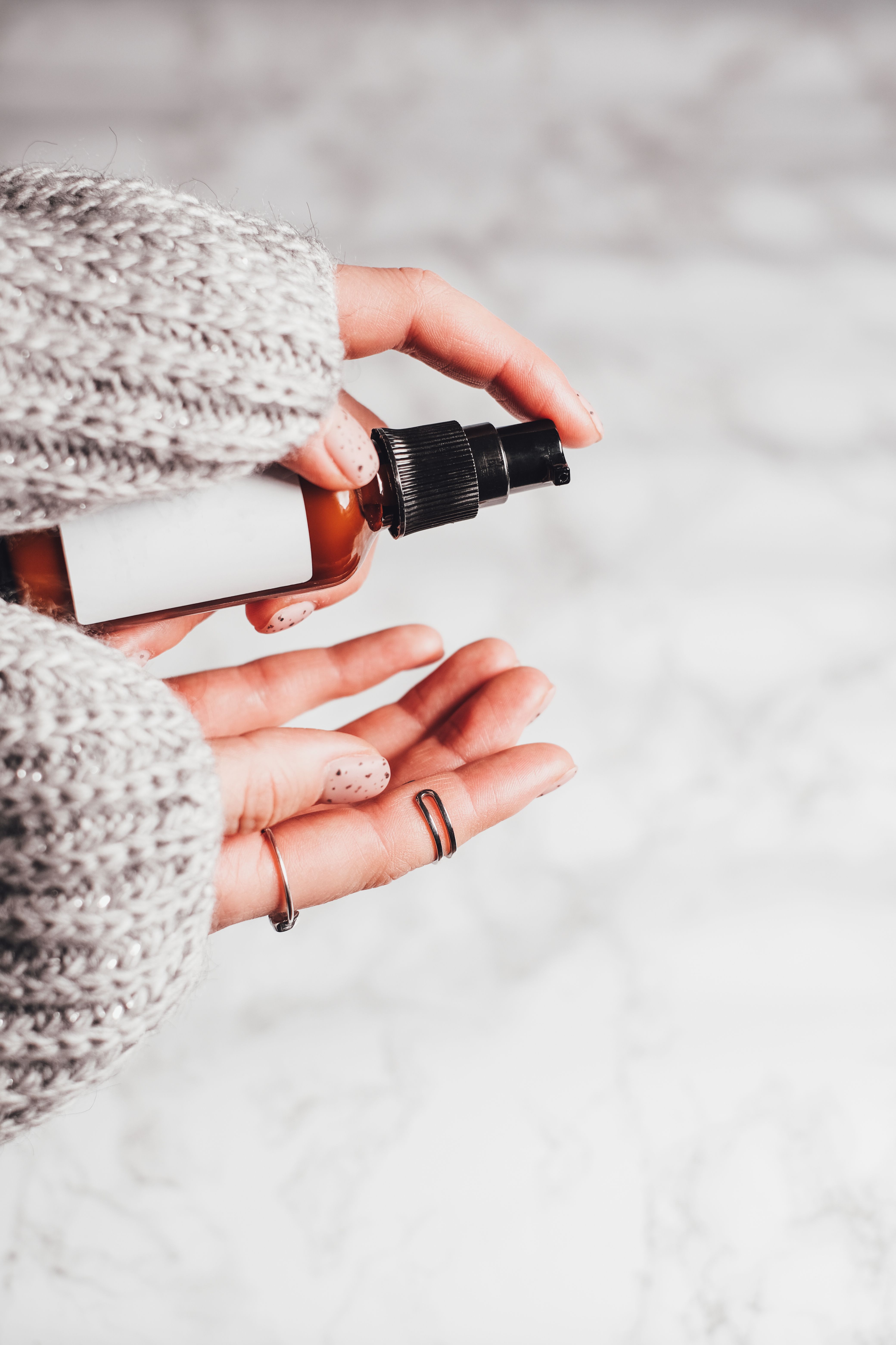 Person in gray knit sweater holding amber dropper bottle with black spray nozzle against snowy background
