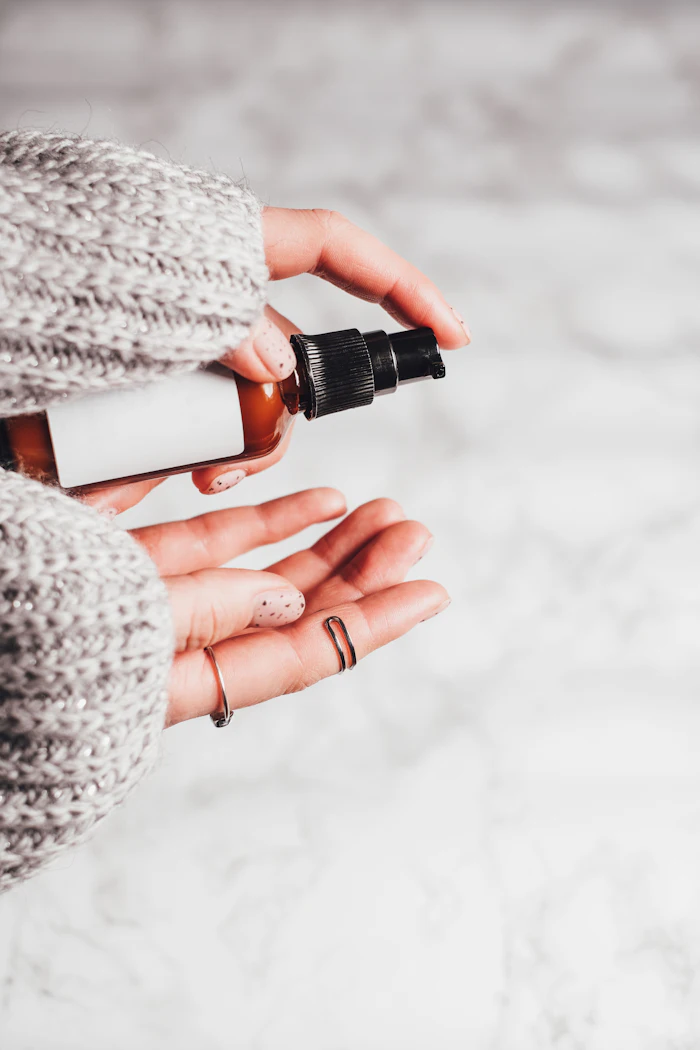 Person in gray knit sweater holding amber dropper bottle with black spray nozzle against snowy background