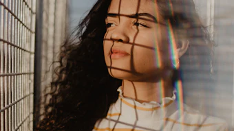 Young woman with long dark curly hair wearing striped shirt, looking upward with grid shadow pattern across face