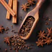 Cinnamon sticks, star anise, and cloves arranged with wooden scoop on dark surface