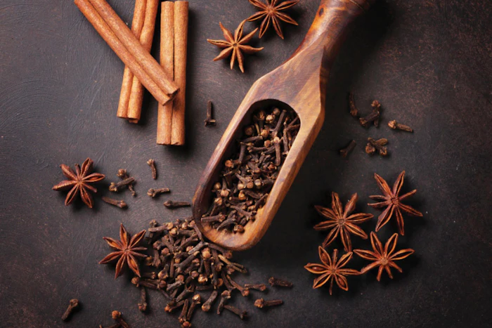 Cinnamon sticks, star anise, and cloves arranged with wooden scoop on dark surface