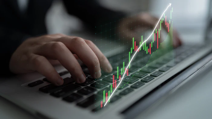 Person typing on laptop displaying financial stock chart with upward trending candlestick graph