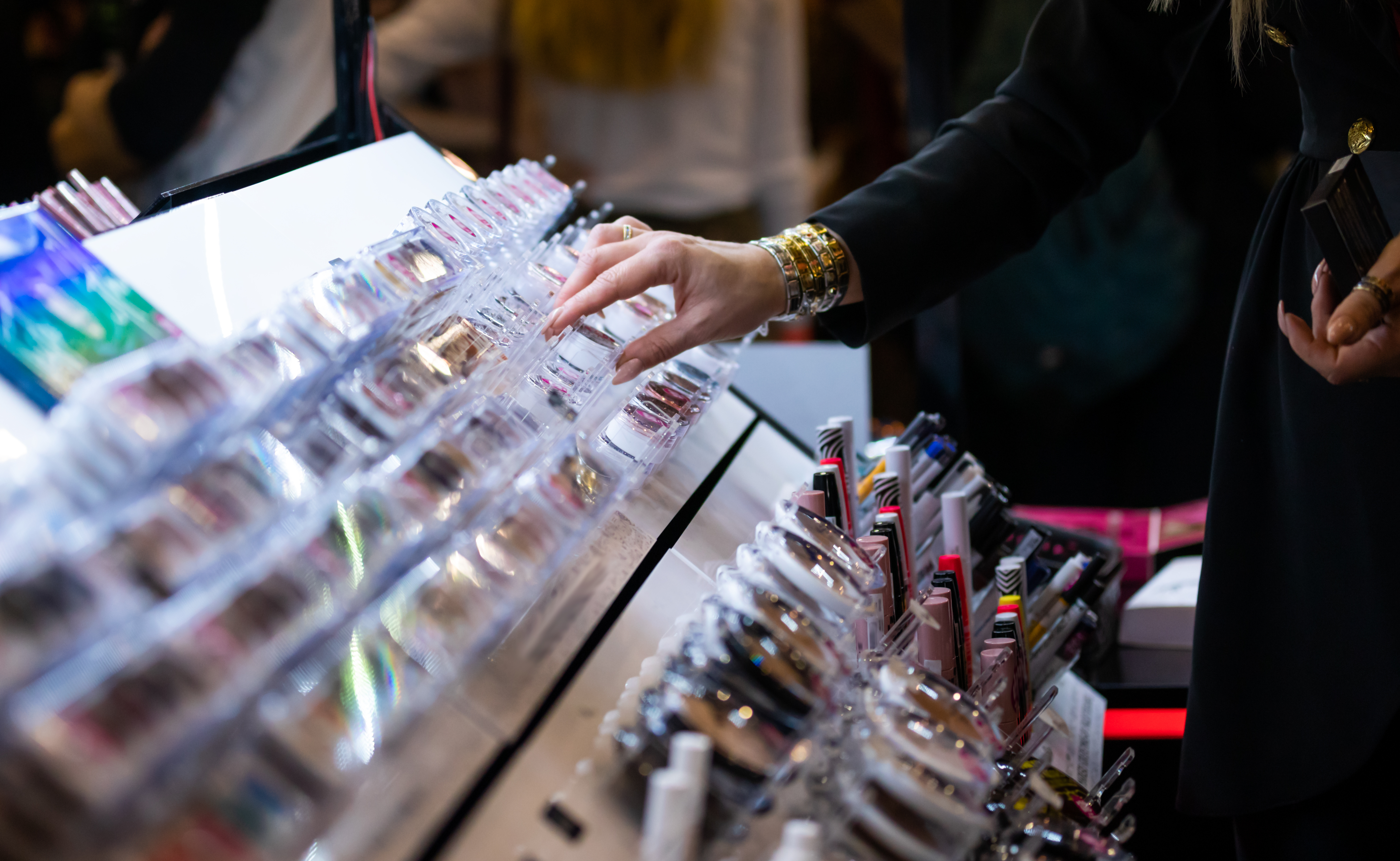 Person browsing cosmetic products displayed on retail counter with multiple colorful beauty items