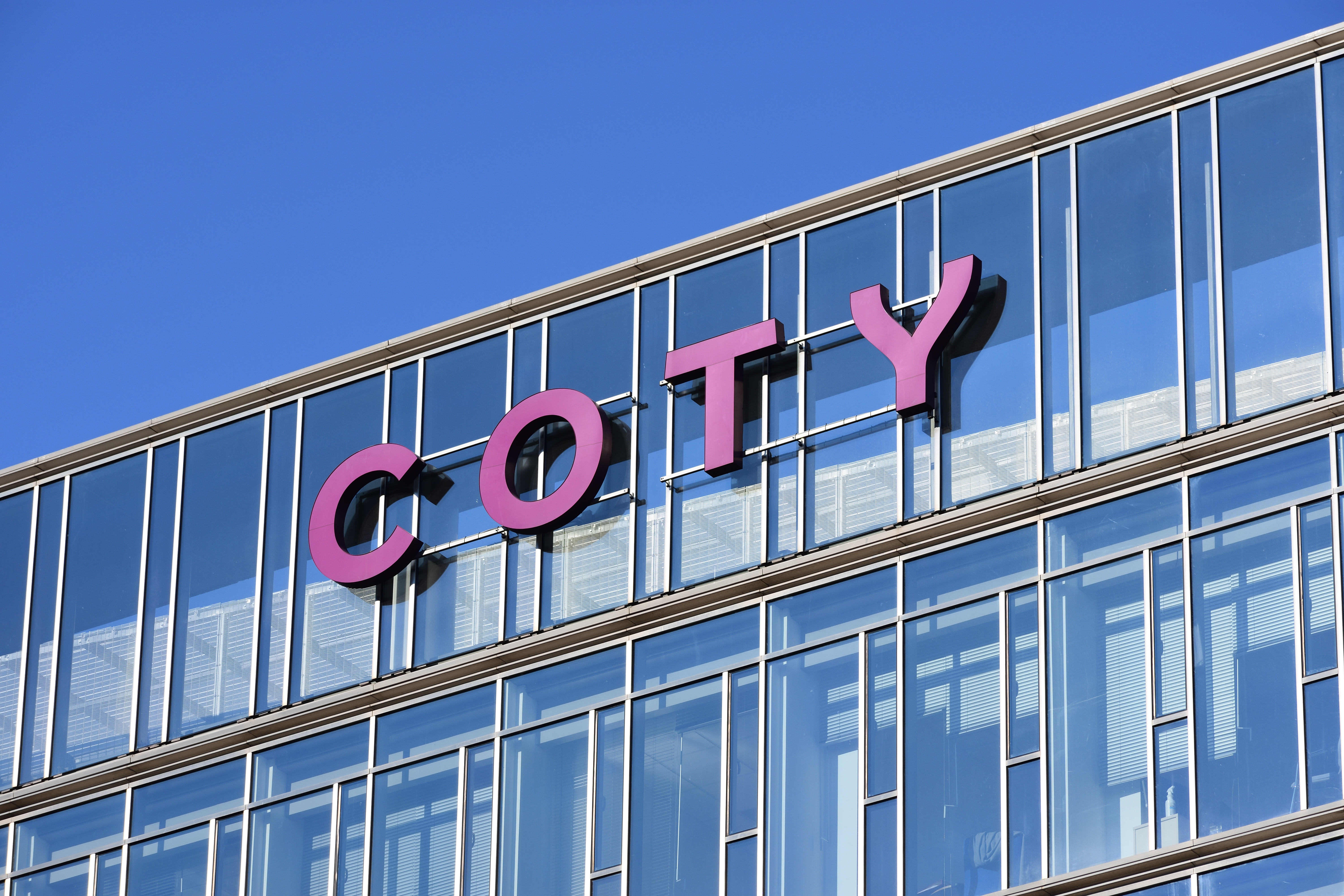 Pink COTY signage on modern glass building facade against blue sky