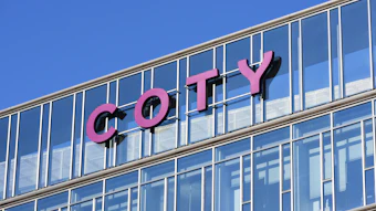 Pink COTY signage on modern glass building facade against blue sky