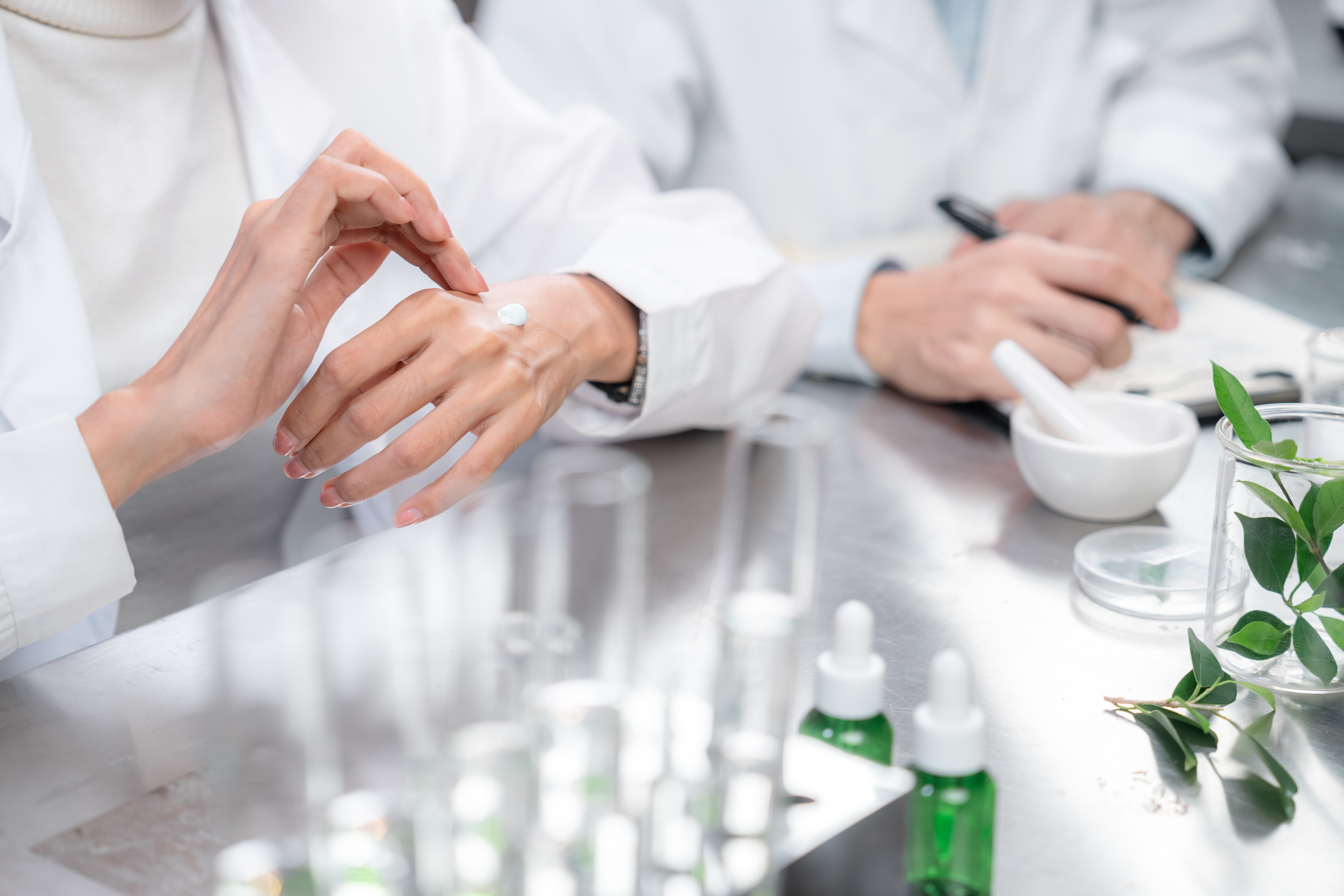 Scientists in lab coats examining skincare products and botanical samples in a laboratory setting
