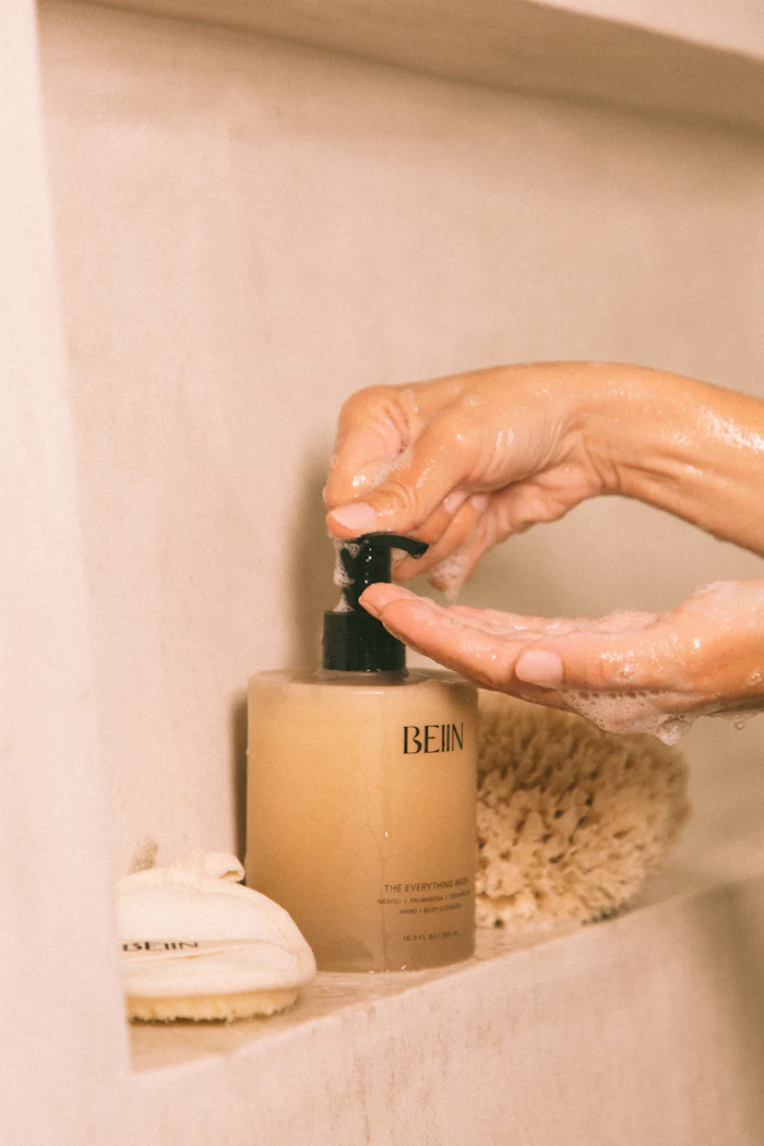 Hands dispensing BEIIN skincare product from pump bottle in bathroom setting