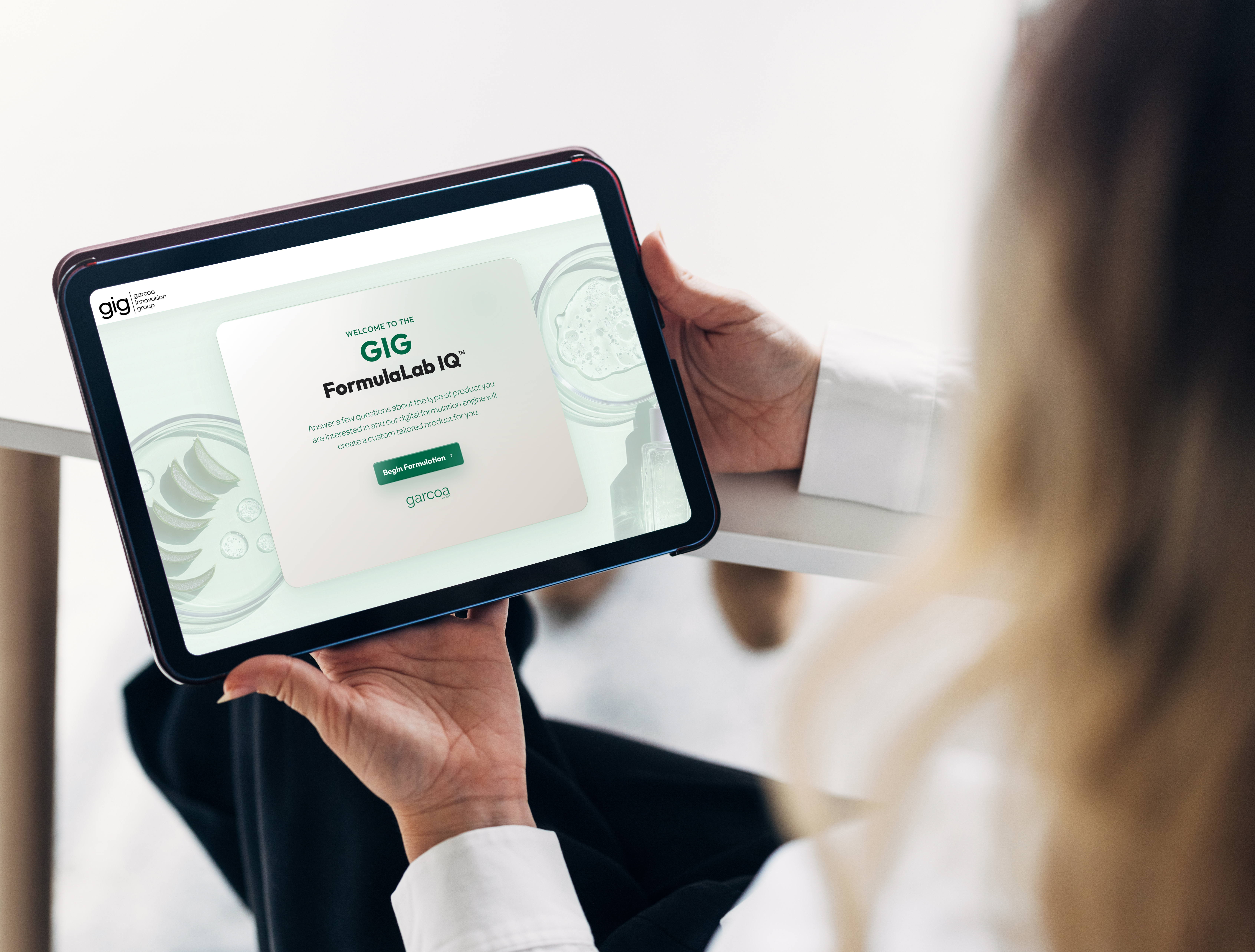 Person holding tablet displaying GIG FormulaLab IQ website with green call-to-action button