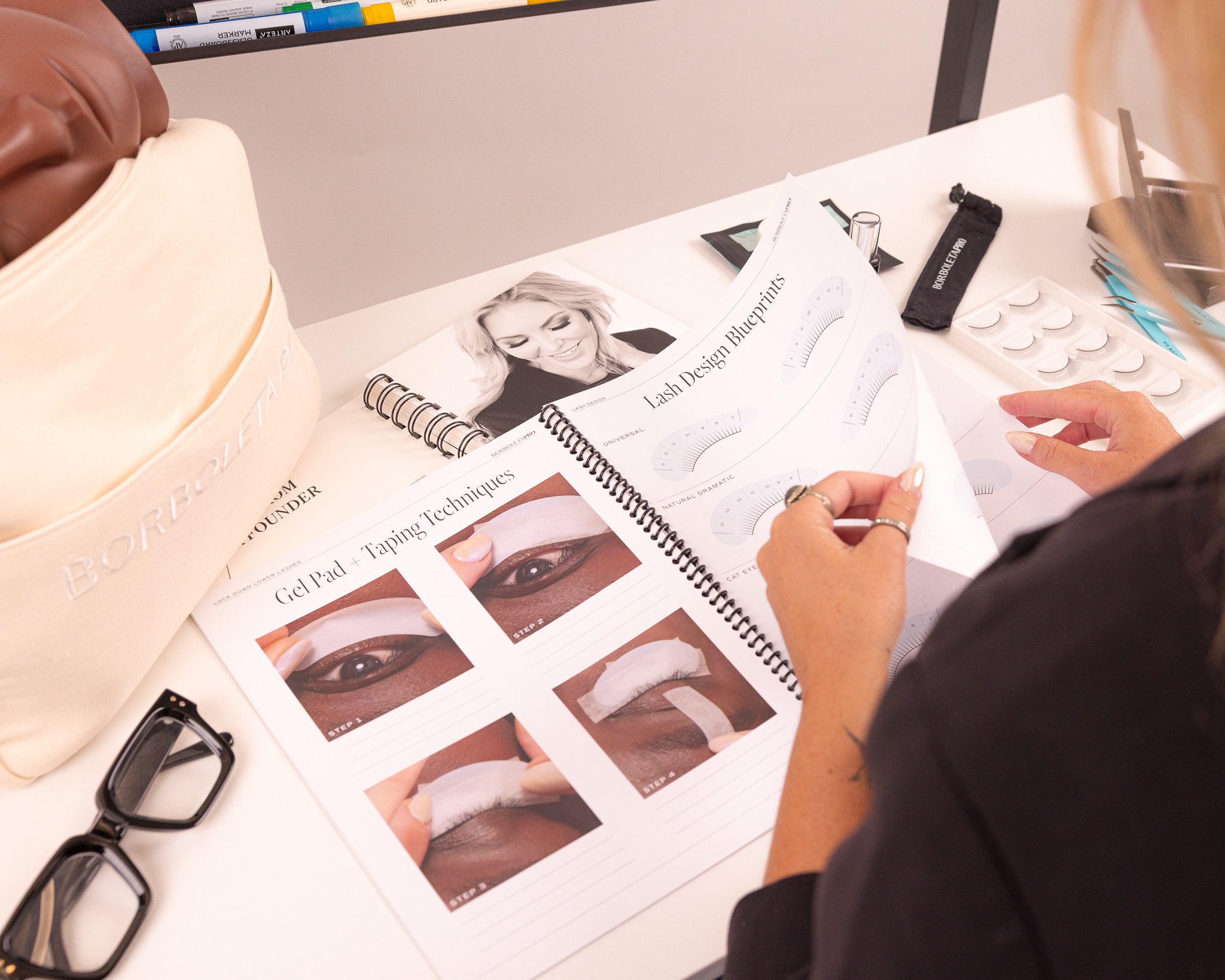 Beauty professional reviewing eyeliner application techniques guide with cosmetic products and samples at workspace