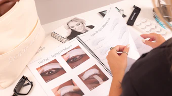 Beauty professional reviewing eyeliner application techniques guide with cosmetic products and samples at workspace