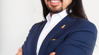 Professional headshot of a man in navy blazer and white shirt, smiling at camera with arms crossed
