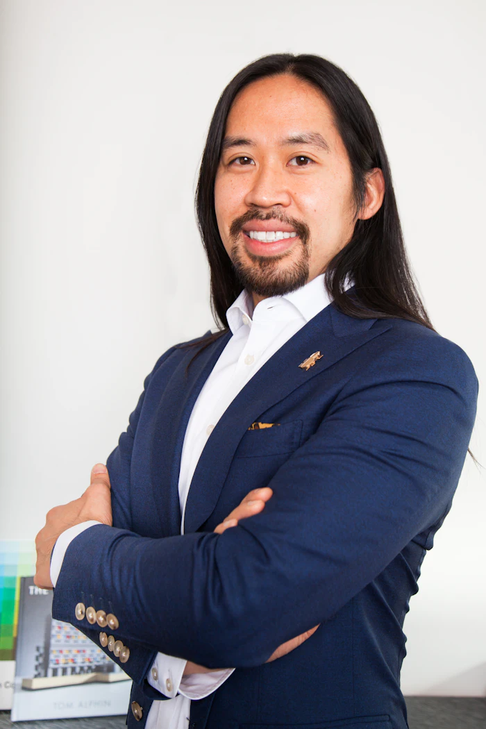 Professional headshot of a man in navy blazer and white shirt, smiling at camera with arms crossed